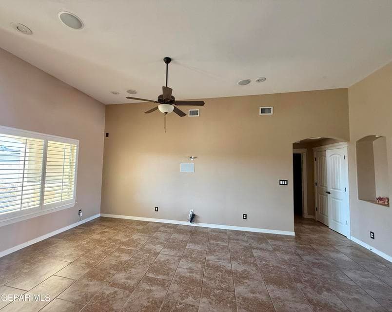 Spacious open living area with tile flooring, built-in speakers, tall ceilings, and natural light.