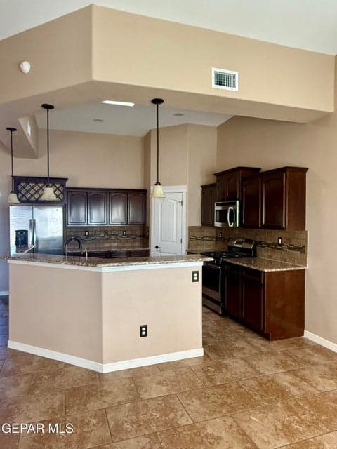 Open kitchen with granite countertops, warm cabinetry, stainless steel appliances, and countertop seating for six.