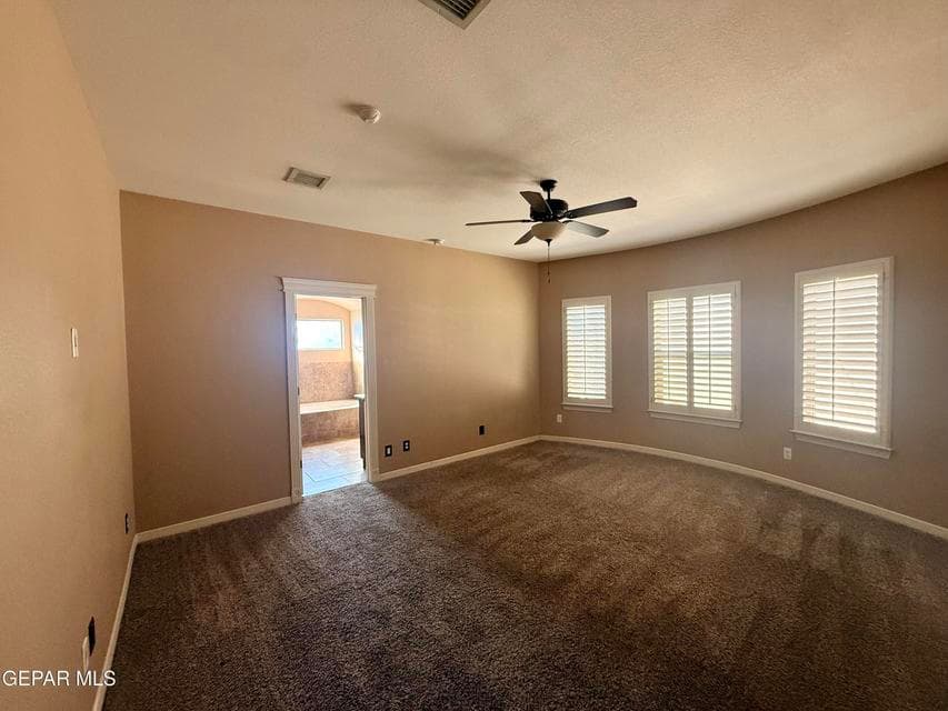Comfortable primary bedroom with carpet flooring, ceiling fan, and shuttered windows.