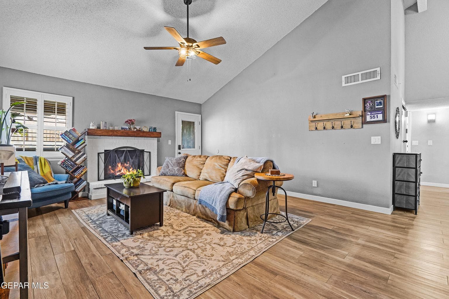 Open layout with a cozy fireplace, wood-like tile flooring, and ceiling fan