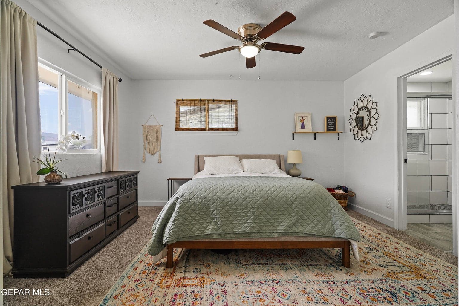Features carpet flooring, large windows, comfortable bed and a ceiling fan