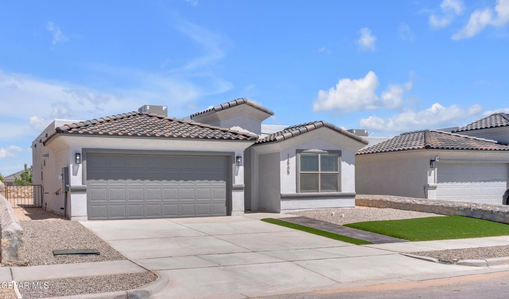 Contemporary stucco exterior featuring a shingle roof, an attached two-car garage, a concrete driveway, and a low-maintenance landscape with artificial turf and gravel