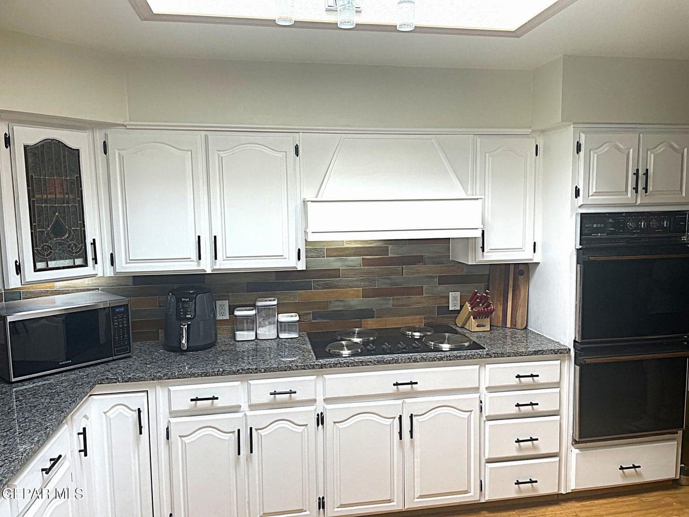 White cabinetry, black hardware, black double wall oven, dark speckled countertops, and a multi-toned backsplash