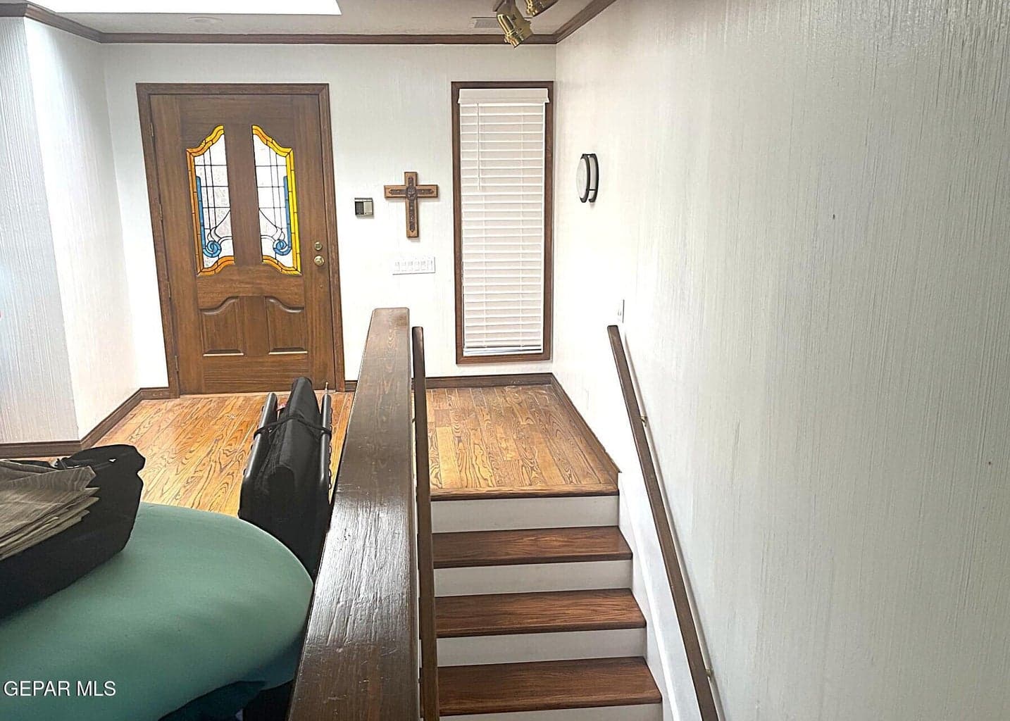 Hardwood flooring, wood-finish staircase with white risers, wood-paneled door with stained glass inserts, and wood window trim