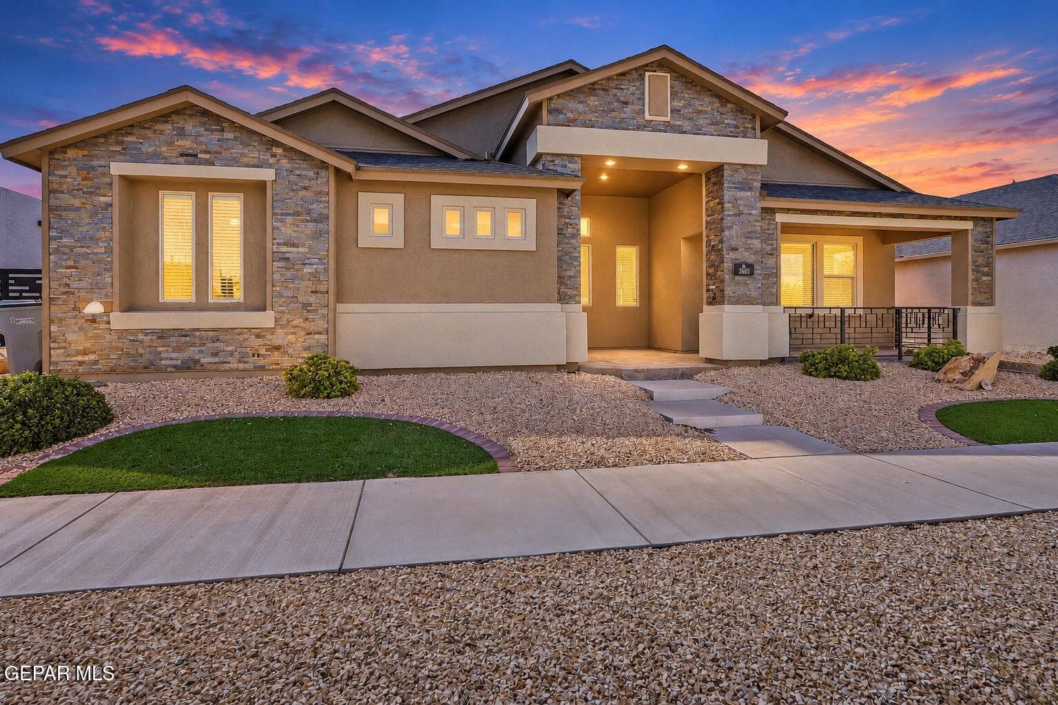 Stucco and stacked stone exterior with a covered entry, a covered porch with decorative railing, a concrete walkway, and a xeriscaped front yard with accent shrubs