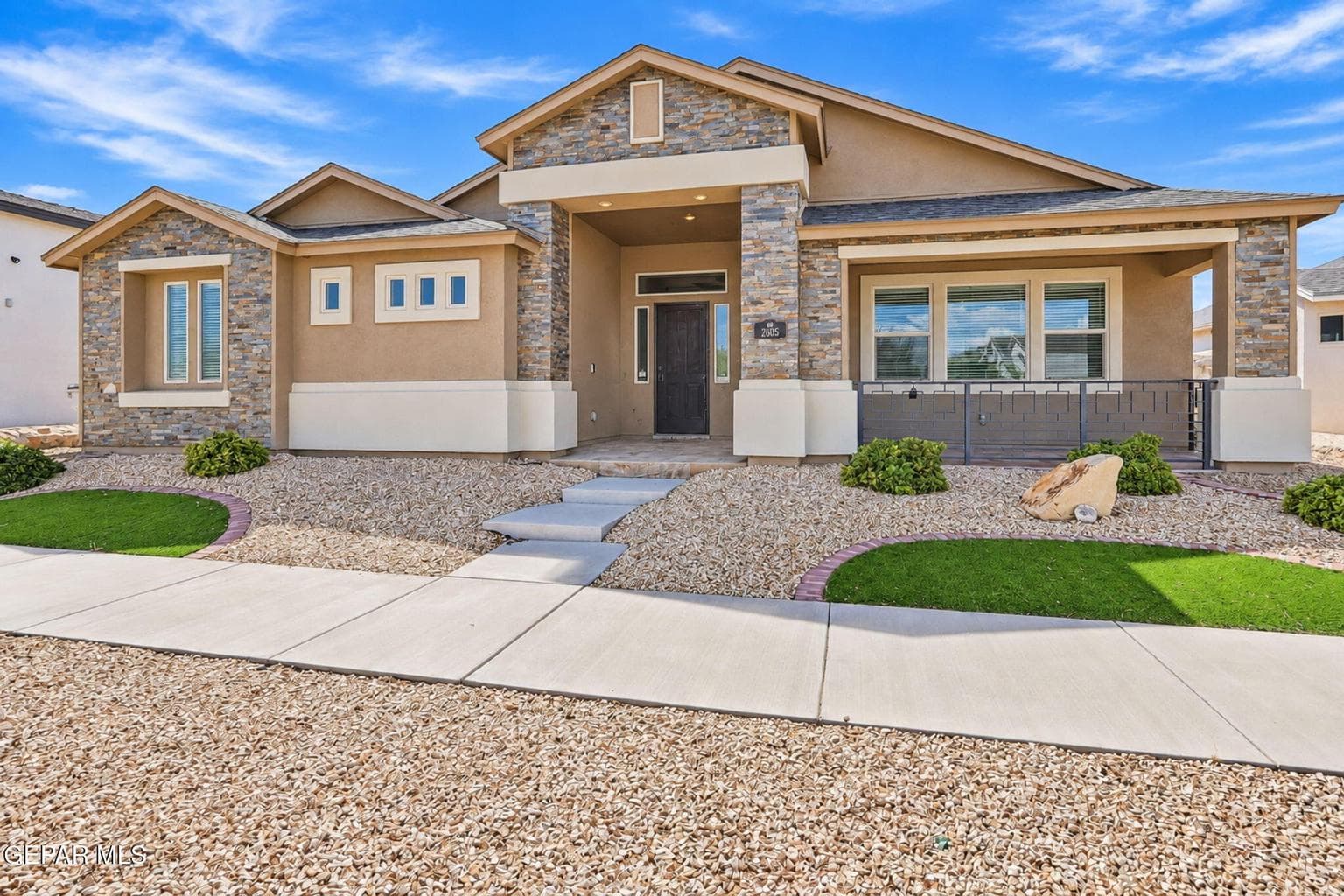 Stucco exterior with stone accents, covered entry, and xeriscaped front yard with artificial turf