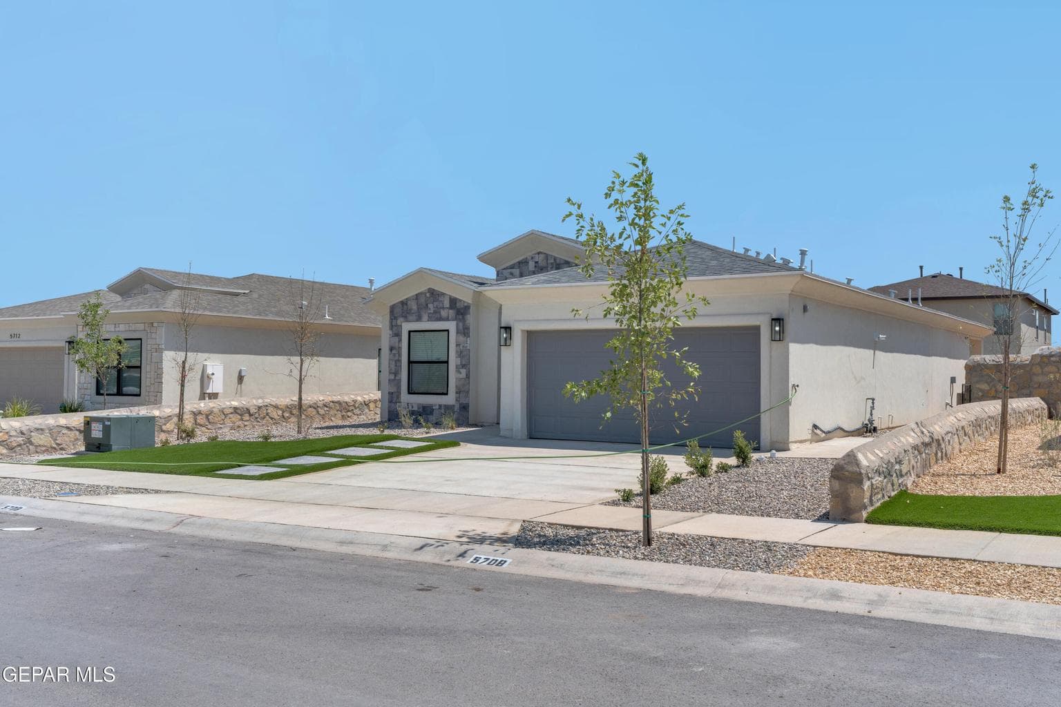 Stucco exterior with stone accents, attached garage, concrete driveway, and artificial turf landscaping with decorative pavers