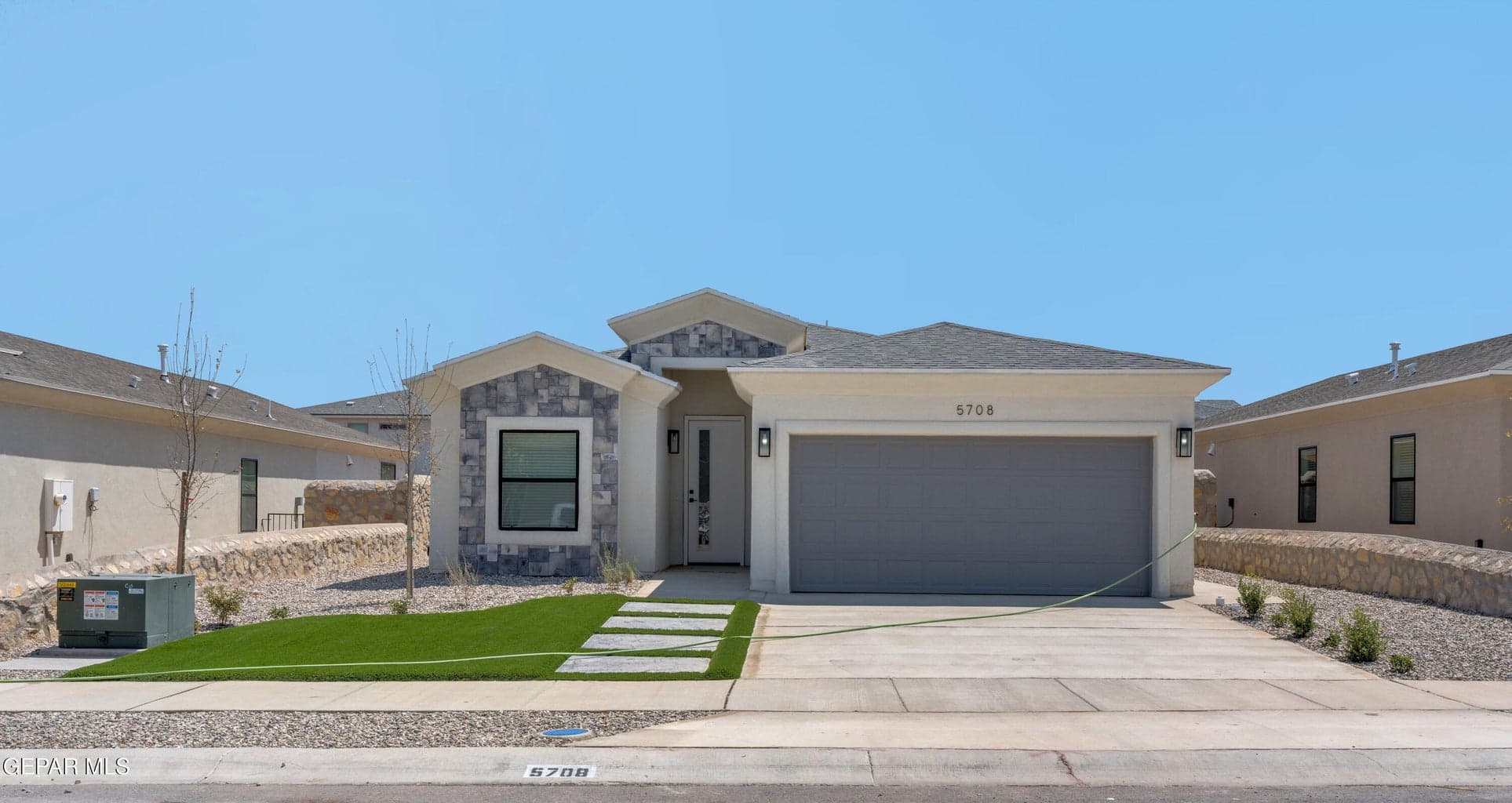 Stucco exterior with stone accents, attached two-car garage, concrete driveway, artificial turf lawn, and stone paver walkway