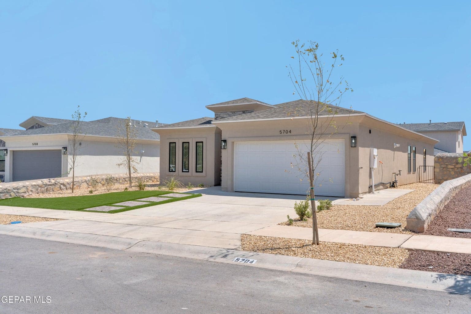 Contemporary stucco exterior with a two-car garage, concrete driveway, and artificial turf landscaping with stepping stones