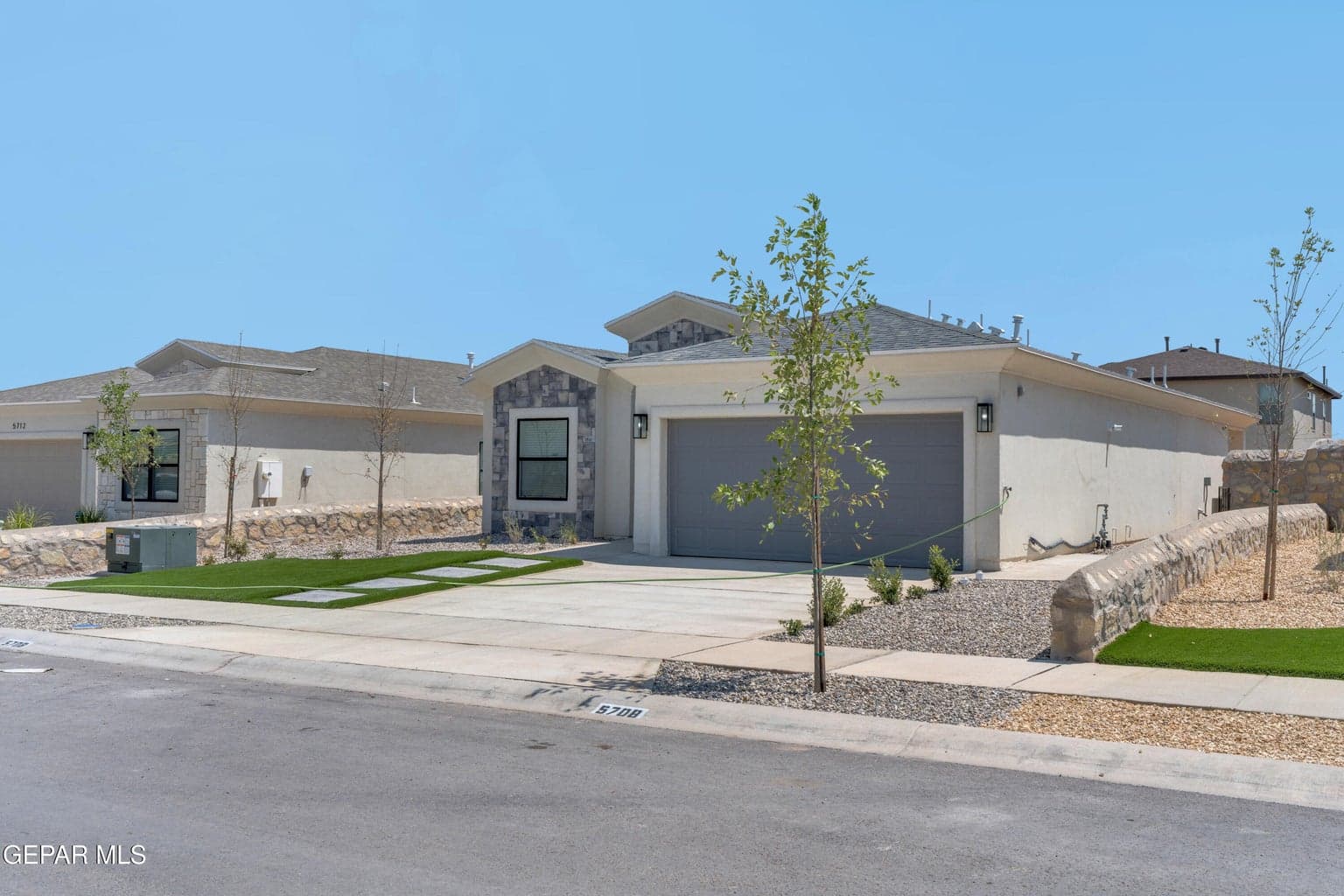 Stucco exterior with stone accents, attached garage, concrete driveway, and artificial turf landscaping with decorative pavers
