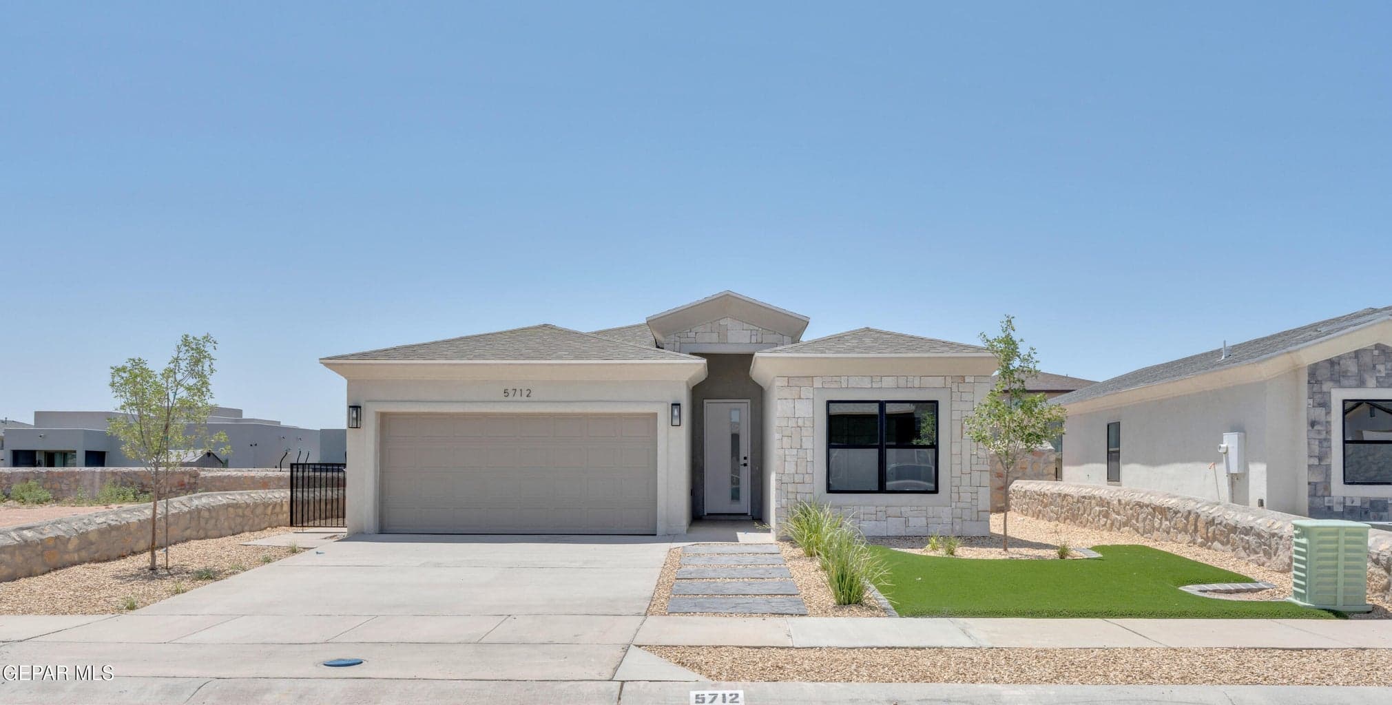 Contemporary exterior with a stone and stucco finish, an attached garage, a paved driveway, and artificial turf landscaping