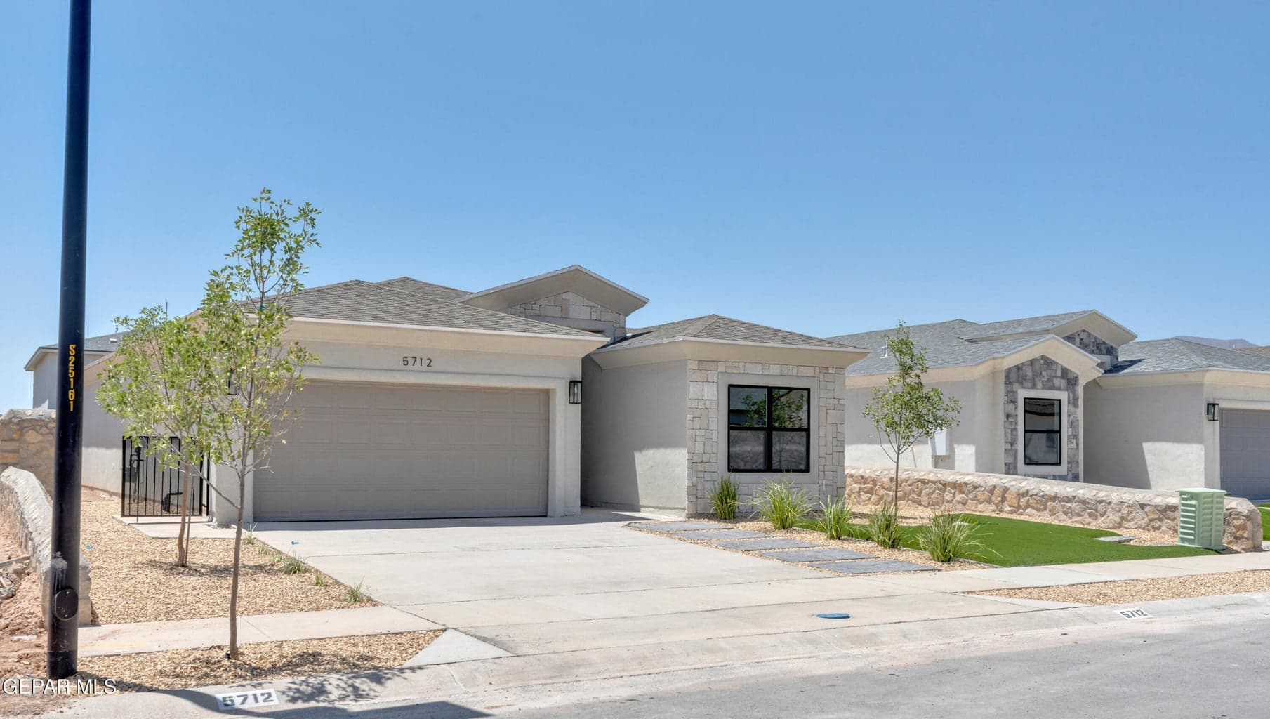 Stucco exterior with stone accents, attached garage, concrete driveway, and a low-maintenance landscape