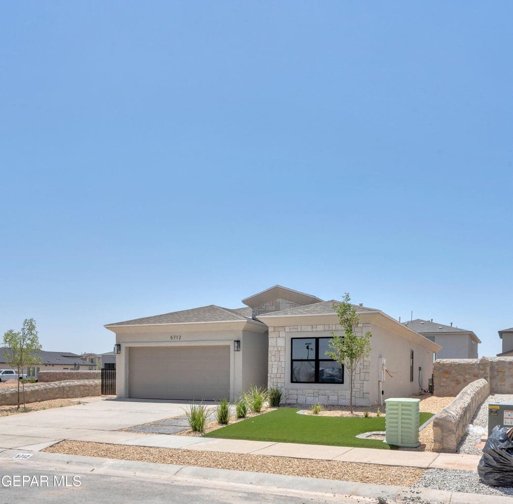 Stucco exterior with stone accents, attached garage, concrete driveway, xeriscaped front yard, and a stone retaining wall