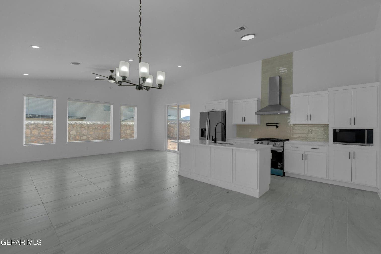 Open-concept living space with large format tile flooring, a modern chandelier, recessed lighting, and a kitchen island with sink
