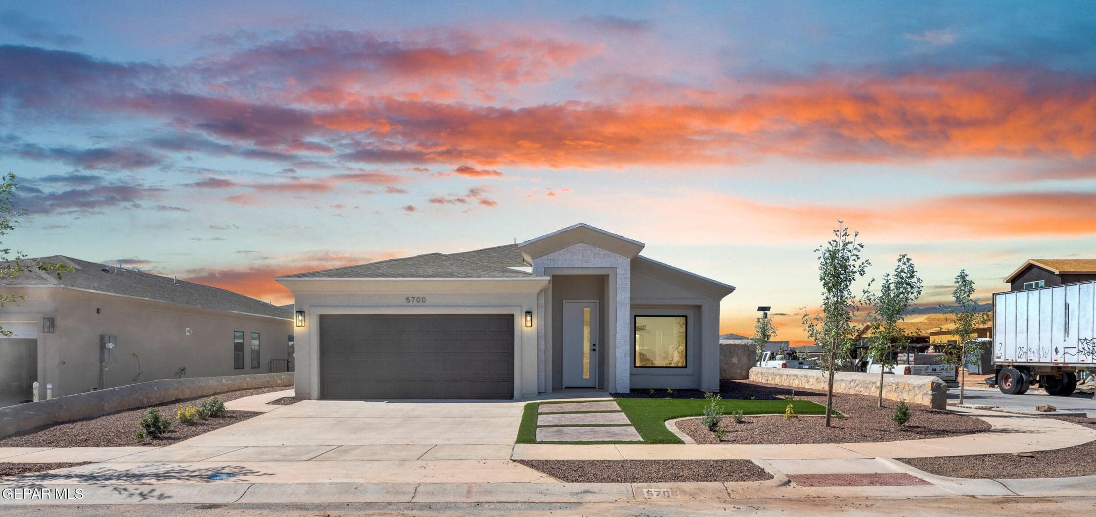 Modern stucco exterior with an attached garage, xeriscape landscaping, concrete paver pathway, and a covered entry