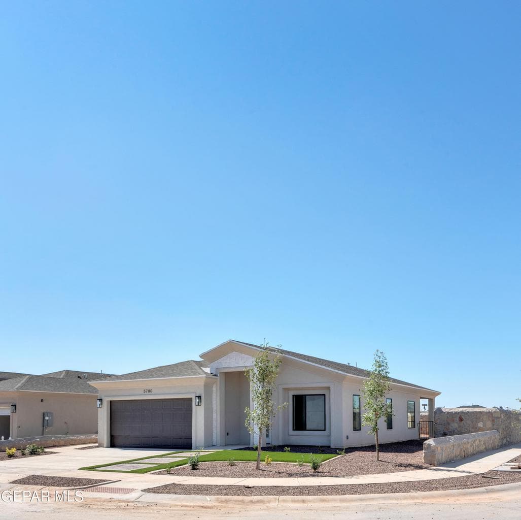 Modern stucco exterior with an integrated garage, covered entry, front landscaping, and a stone wall