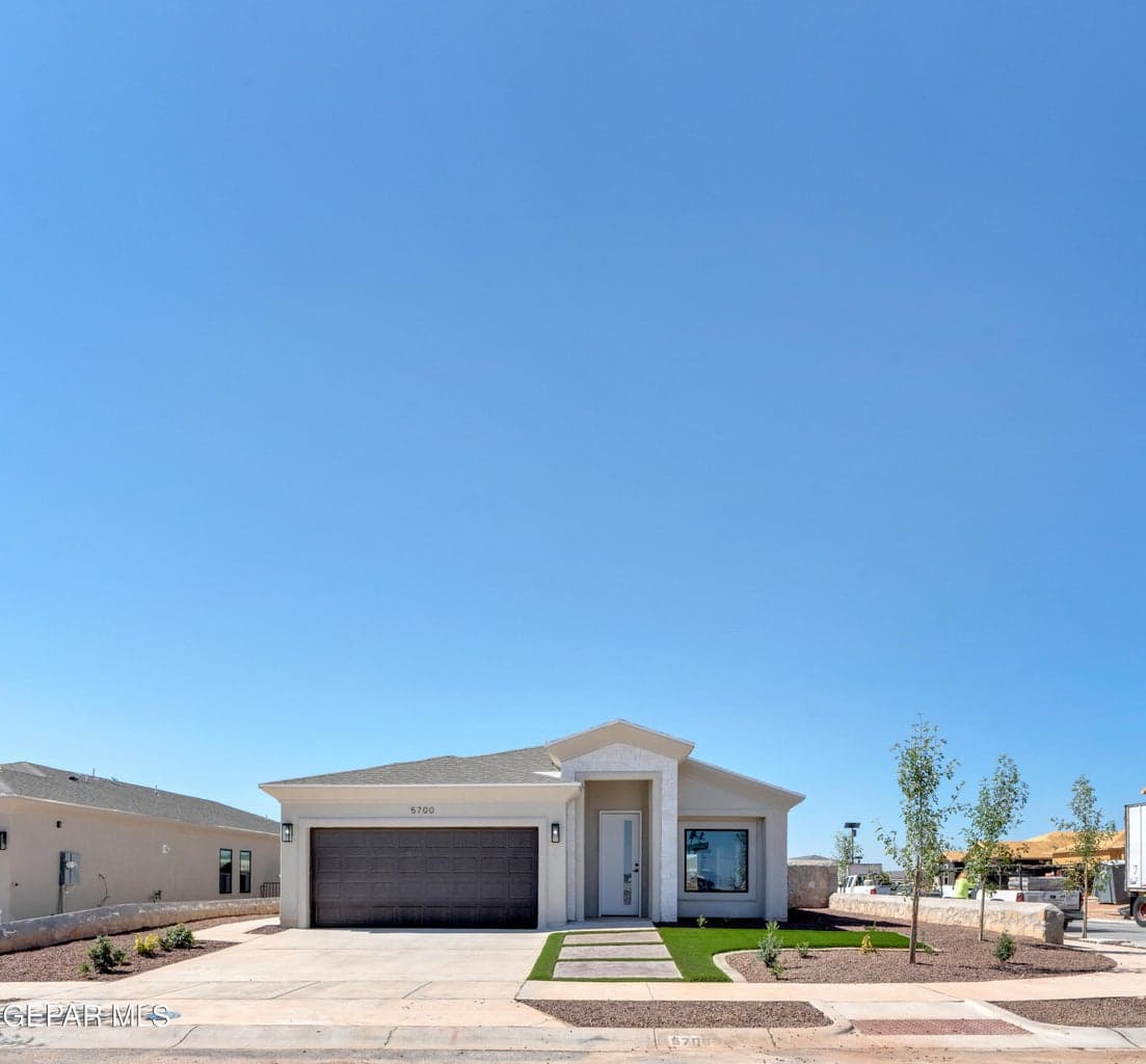Single-story residence featuring a two-car garage, concrete driveway, and a front yard with artificial turf and stepping stones