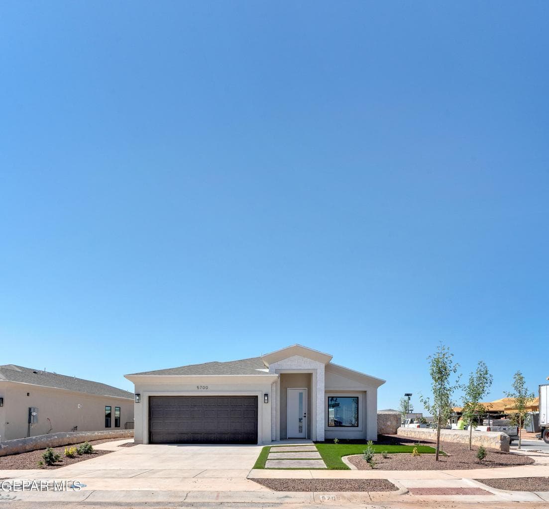 Single-story residence featuring a two-car garage, concrete driveway, and a front yard with artificial turf and stepping stones