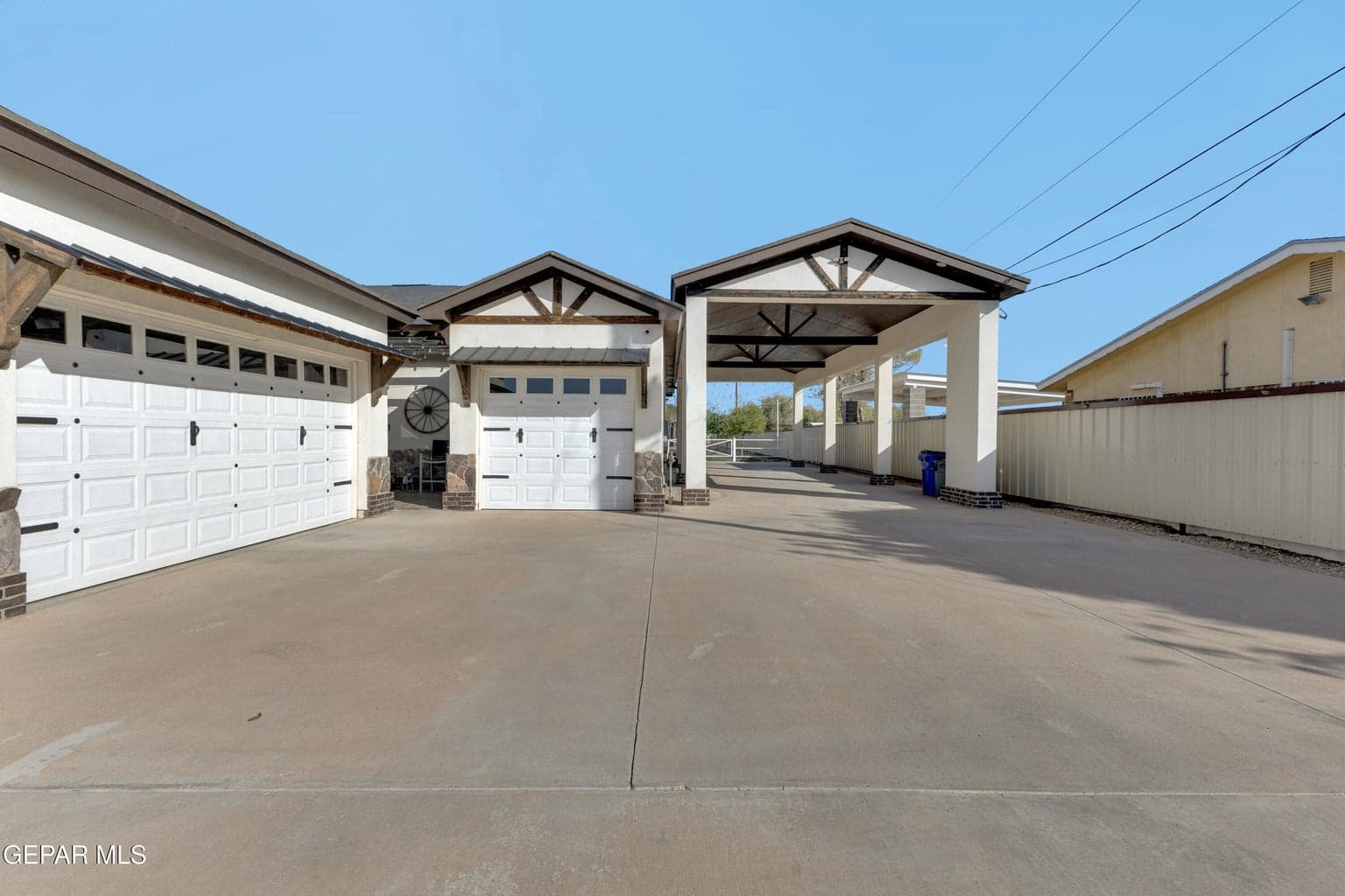 Driveway with an attached carport structure, multiple garage doors with decorative hardware, and stone column accents