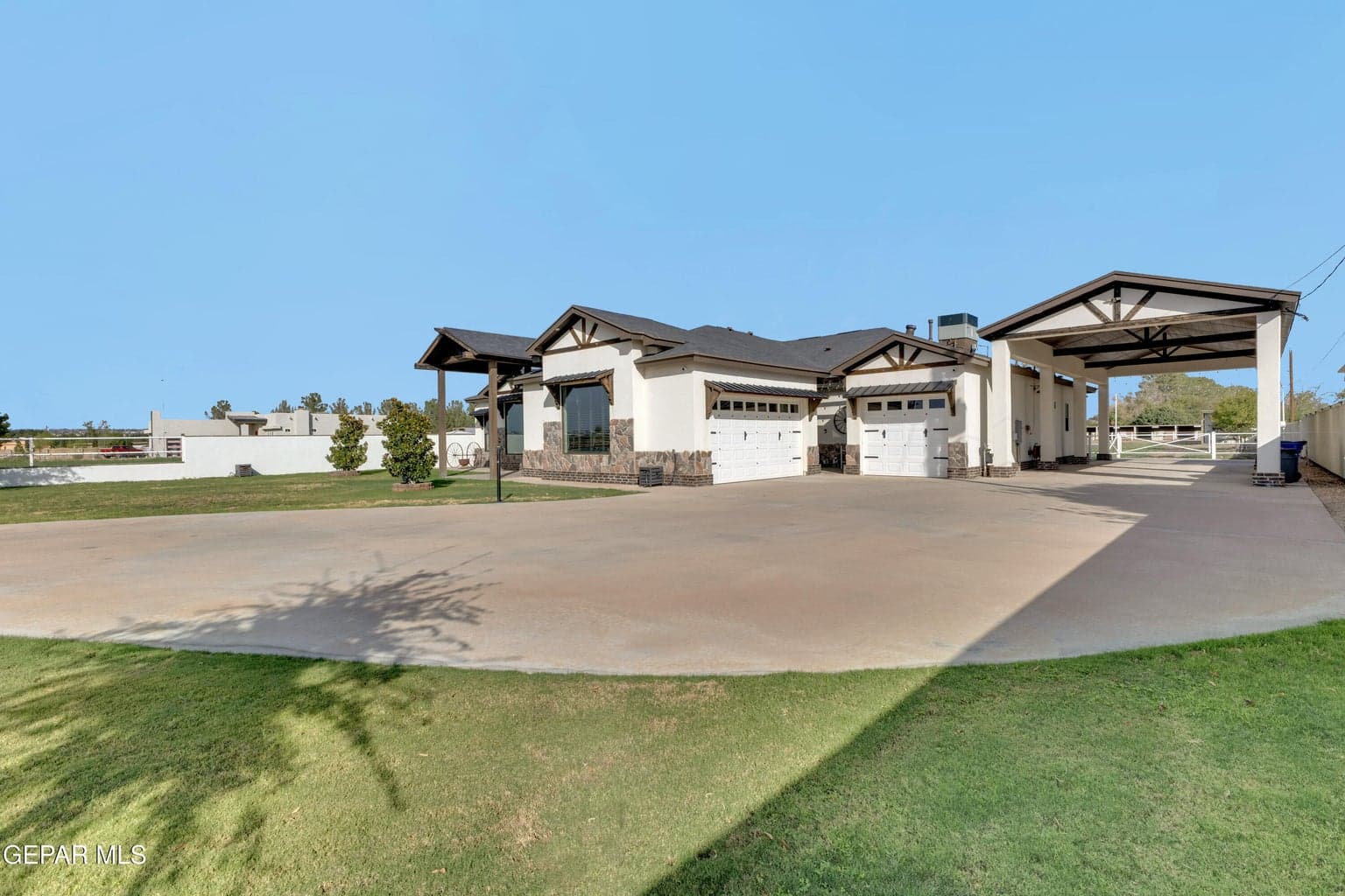 Exterior featuring a stone facade, stucco finish, multiple garage doors, covered portico, and expansive paved driveway