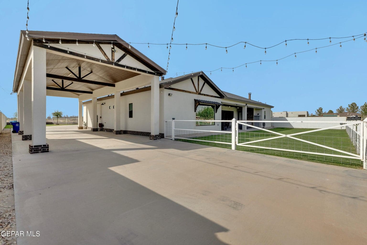 Extended covered parking structure with wood-beam accents, a paved driveway, and a fenced yard