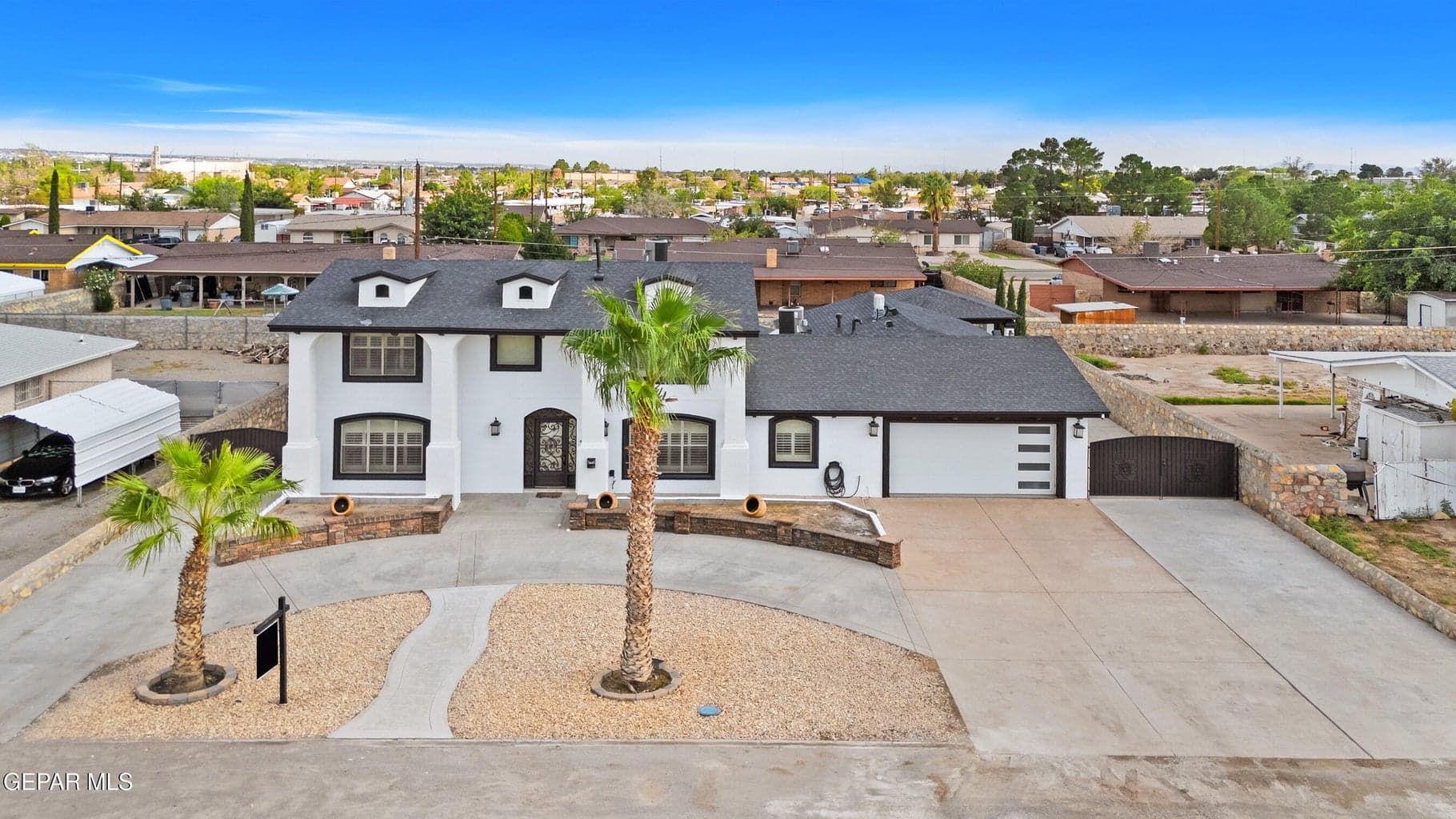 White stucco exterior with black trim, concrete driveway, attached garage, and decorative iron entry gate