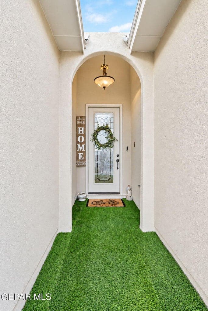 Arched entryway with a decorative light fixture, leading to a glass-paneled entry door
