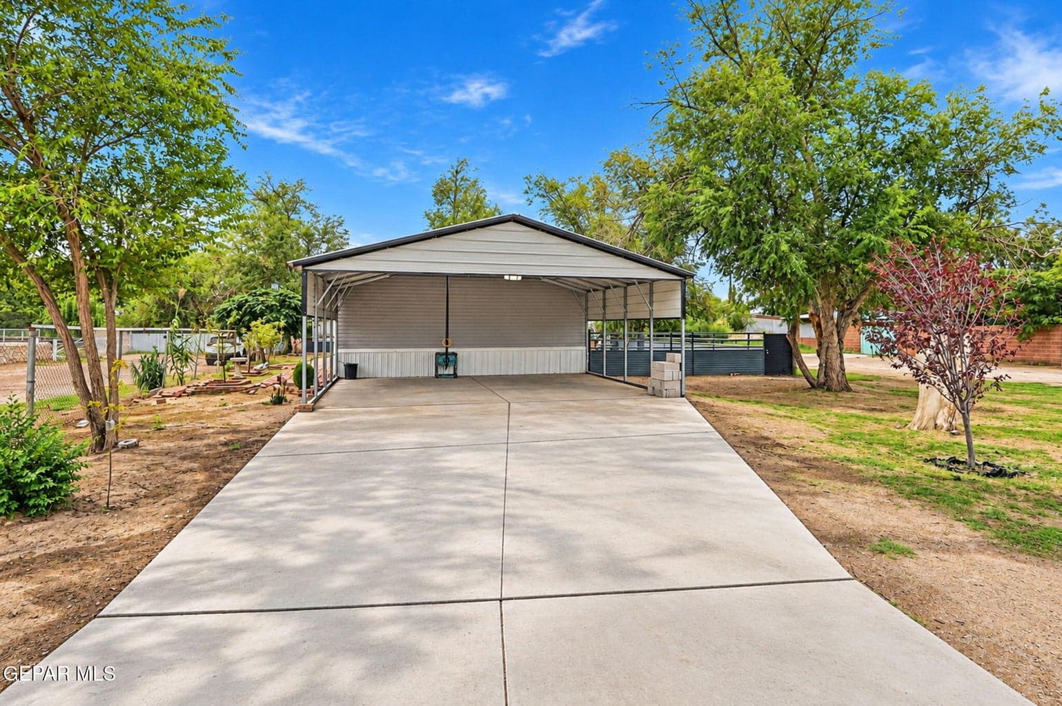 Concrete driveway leading to a metal carport structure with a gray facade
