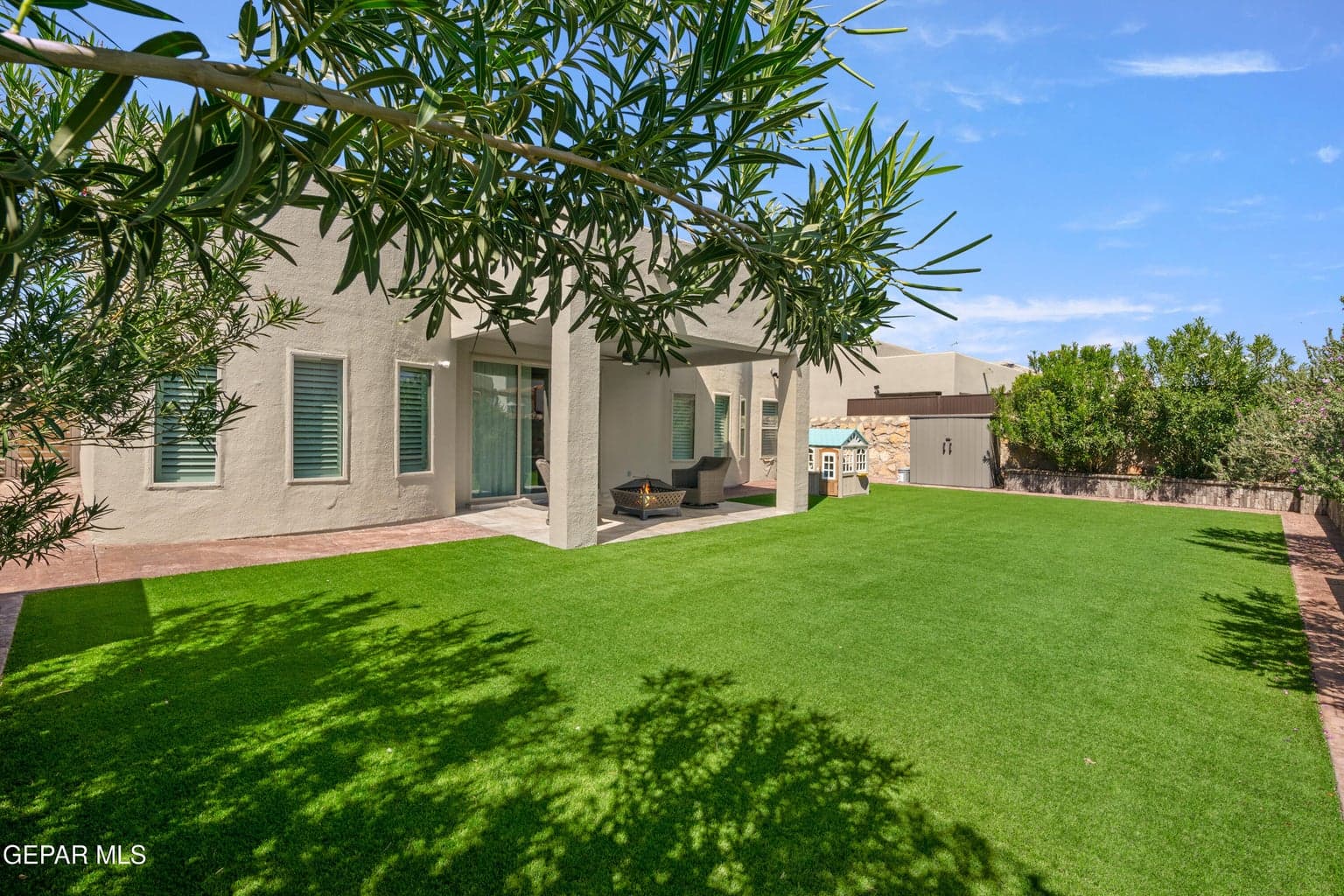Spacious backyard featuring artificial turf, a covered patio, stucco exterior, and a privacy wall with mature landscaping