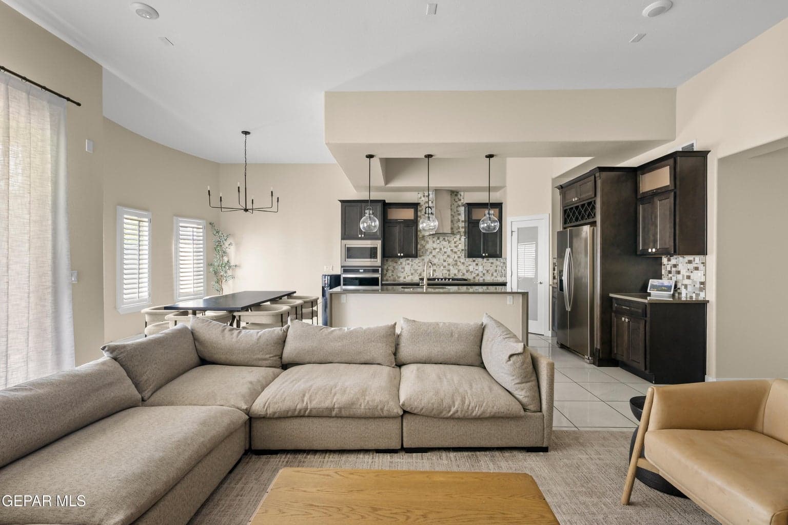 High ceilings showcasing a contemporary chandelier, plantation shutters, dark wood-finish cabinetry, stainless steel appliances, and a tiled kitchen backsplash