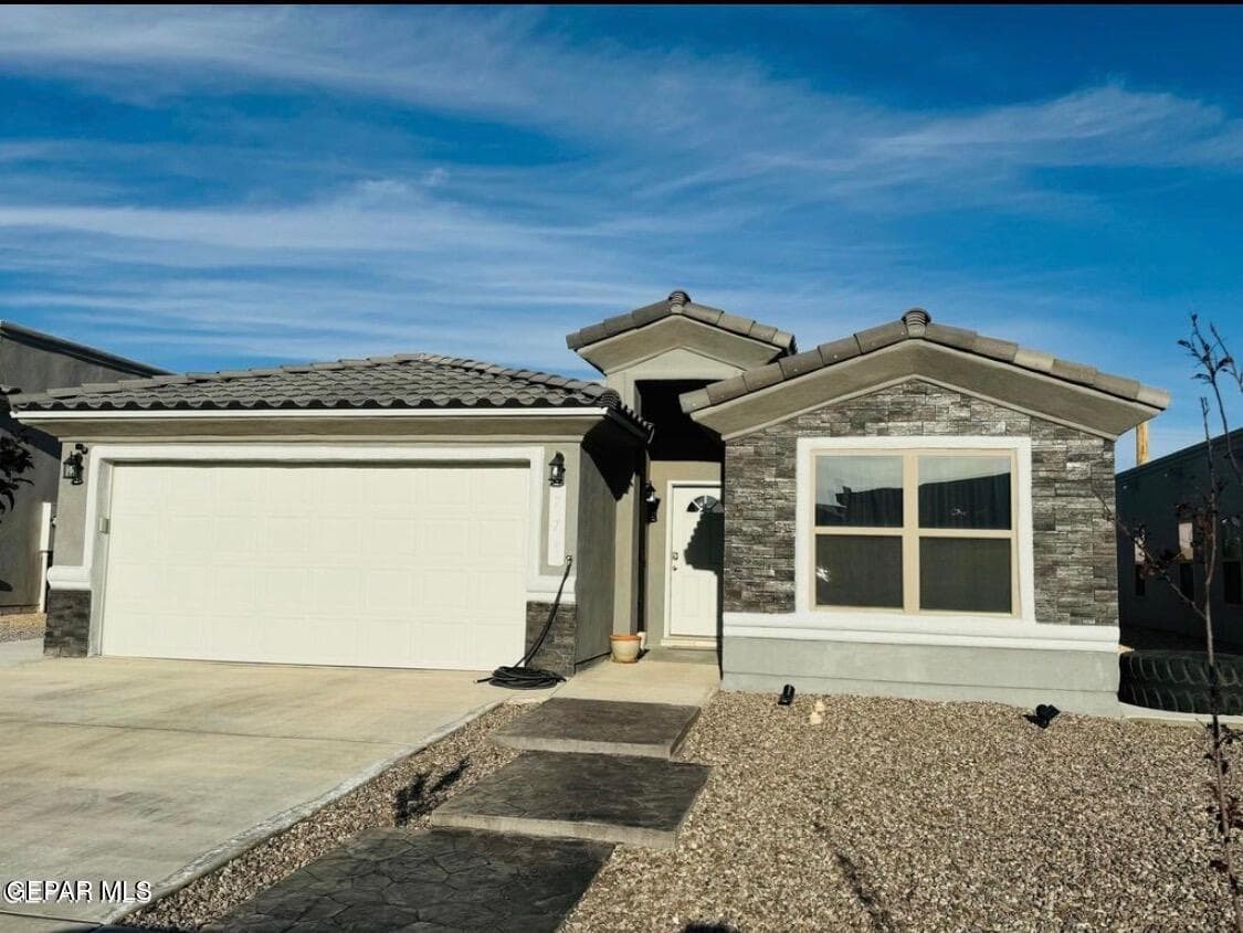 Textured tile roof, stone veneer accents, integrated two-car garage, concrete driveway, and stamped concrete pathway