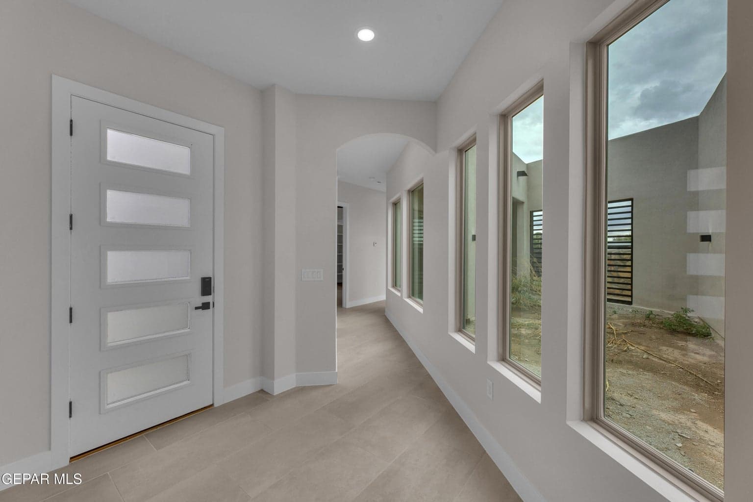 Modern entry door with frosted glass panels, recessed ceiling lighting, arched hallway entry, and floor-to-ceiling windows