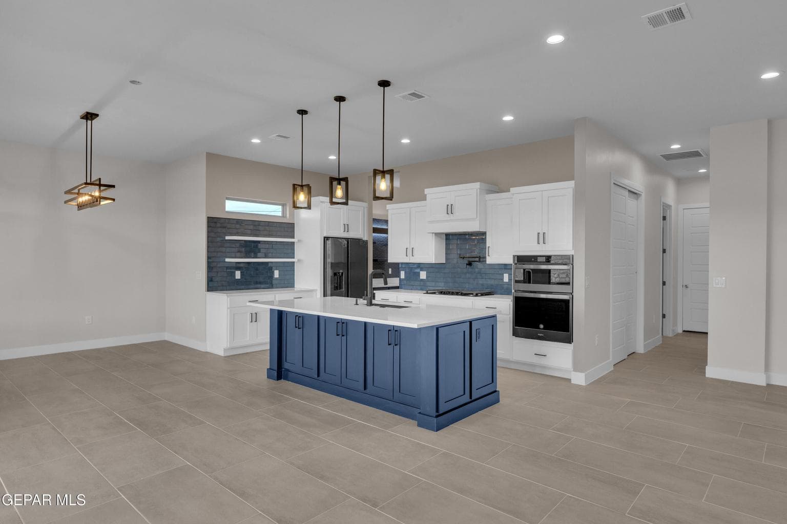 Expansive floor tile throughout, bright kitchen with white cabinetry, blue island with pendant lighting, integrated stainless steel appliances, and a tiled backsplash