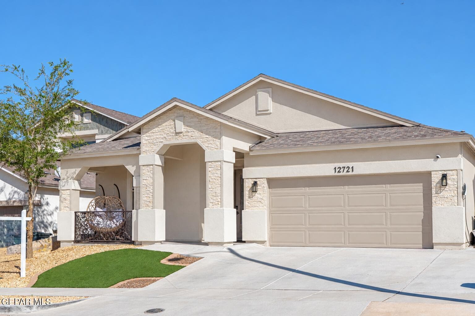 Stucco exterior with stone accents, covered front entry, attached garage, concrete driveway, and low-maintenance landscaping
