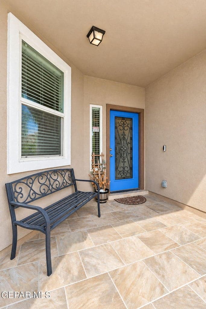 Covered entryway with tile flooring and a vibrant blue door featuring decorative wrought iron