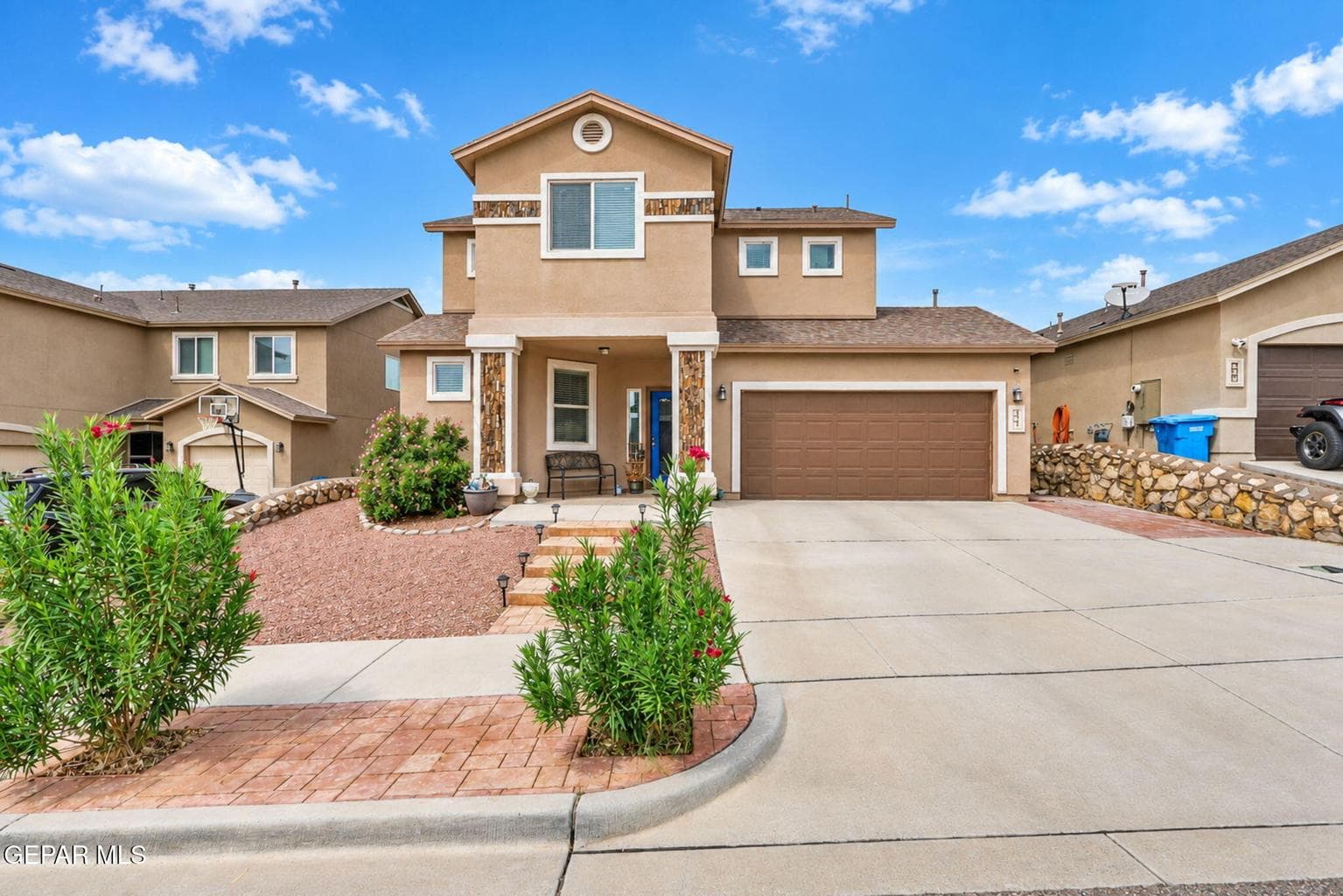 Stucco exterior with a two-car garage, concrete driveway, and brick-accented front walk