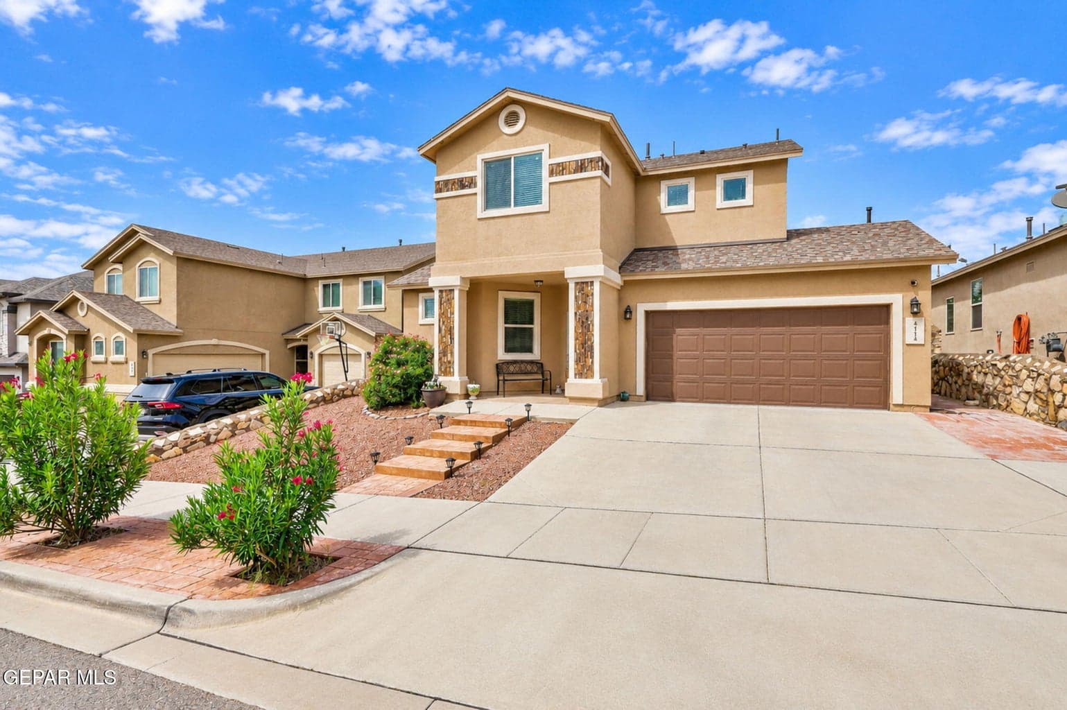 Stucco exterior with decorative stone accents, concrete driveway, and attached garage