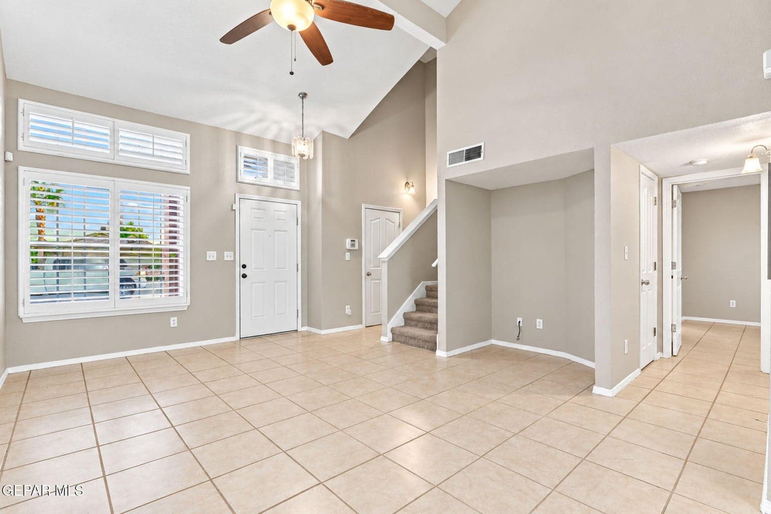 Vaulted ceiling with a ceiling fan, tiled flooring, white plantation shutters, and a carpeted staircase
