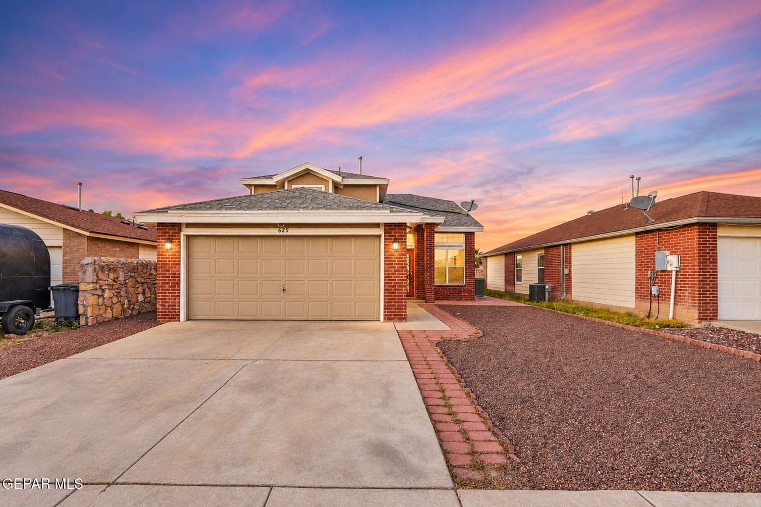 Brick façade, attached two-car garage, concrete driveway, decorative stone landscaping, red brick paver border