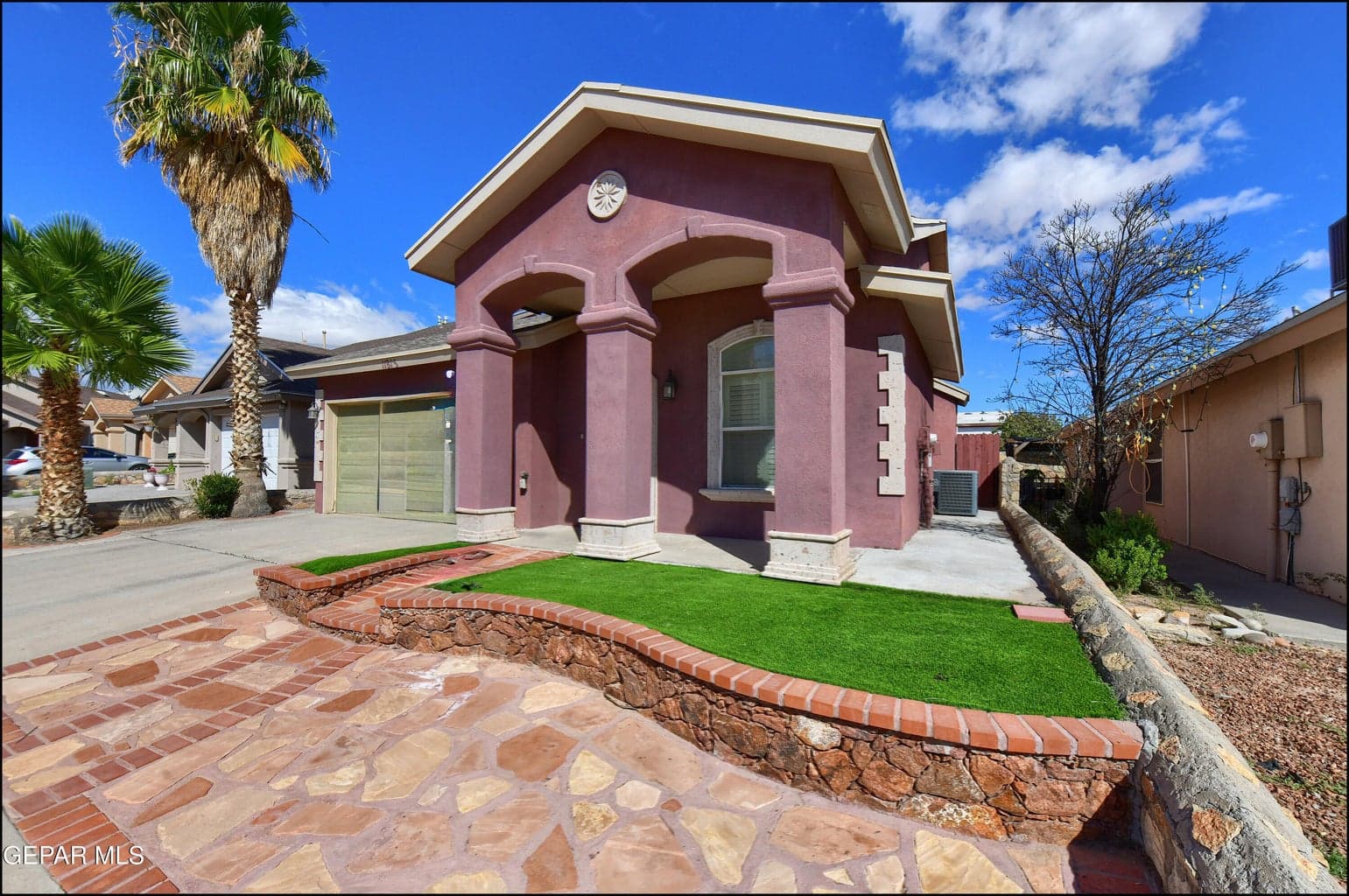 Distinctive residential home featuring a striking mauve exterior with architectural detailing and arched entryway and stone entry front view
