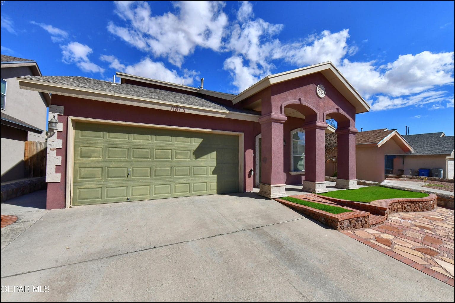 Stucco exterior with an arched entry, attached two-car garage, stone-patterned walkway, and artificial turf landscaping