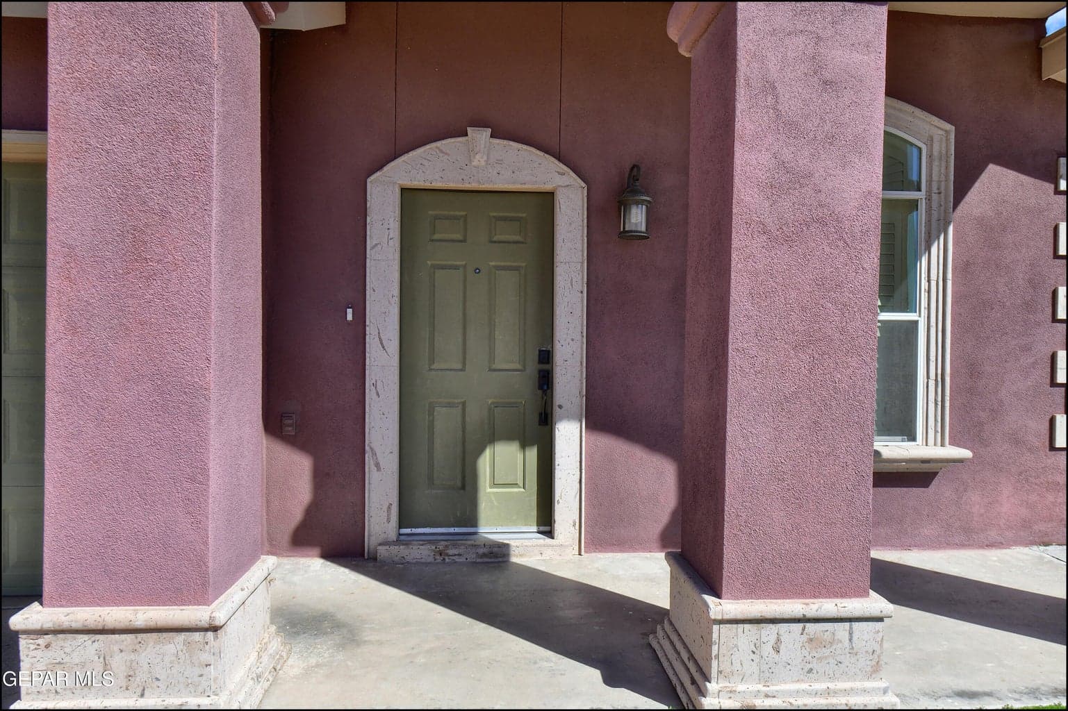 Stucco exterior with a paneled entry door, arched door surround, and decorative exterior lighting
