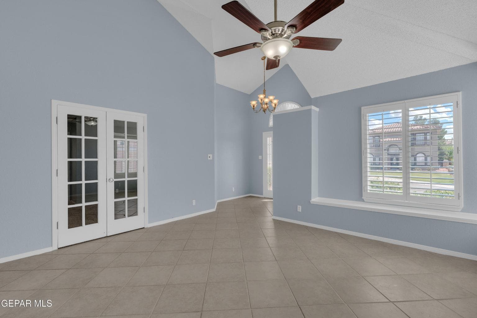 Vaulted ceiling featuring a ceiling fan with integrated lighting, tile flooring, French doors, and a built-in window seat with plantation shutters