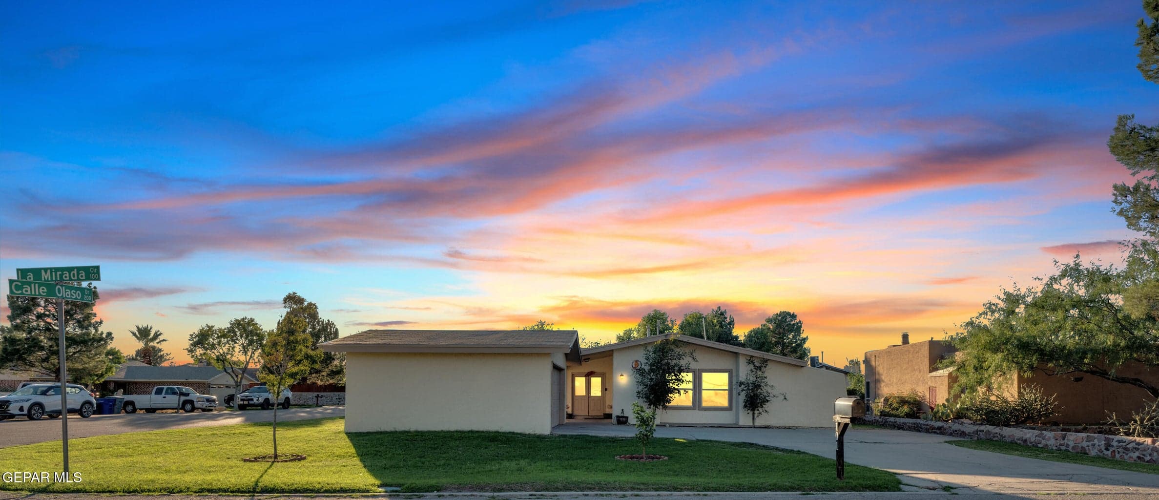 Single-story exterior featuring a light-toned stucco facade, low-slope roofline, attached garage, and a spacious front lawn