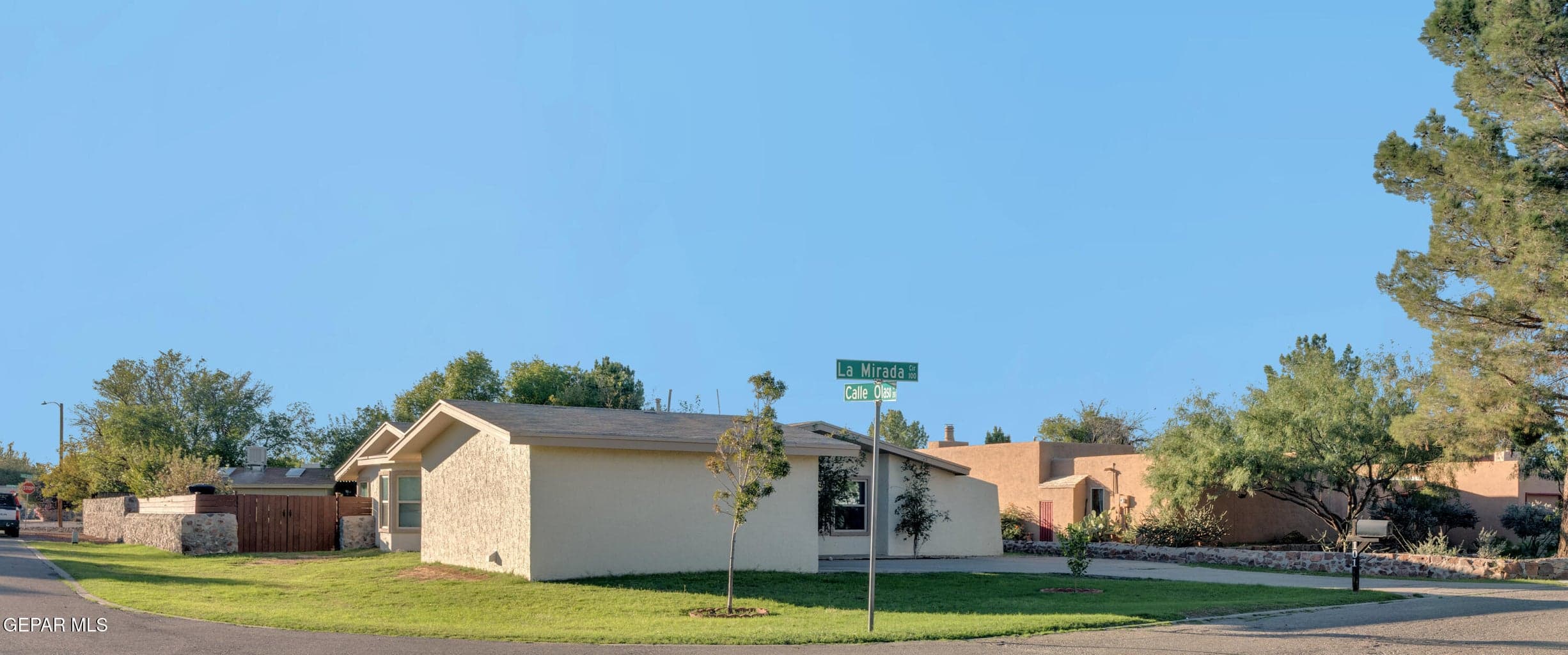 Single-story exterior featuring a light-toned stucco facade, low-pitch roofline, paved driveway, and mature landscaping