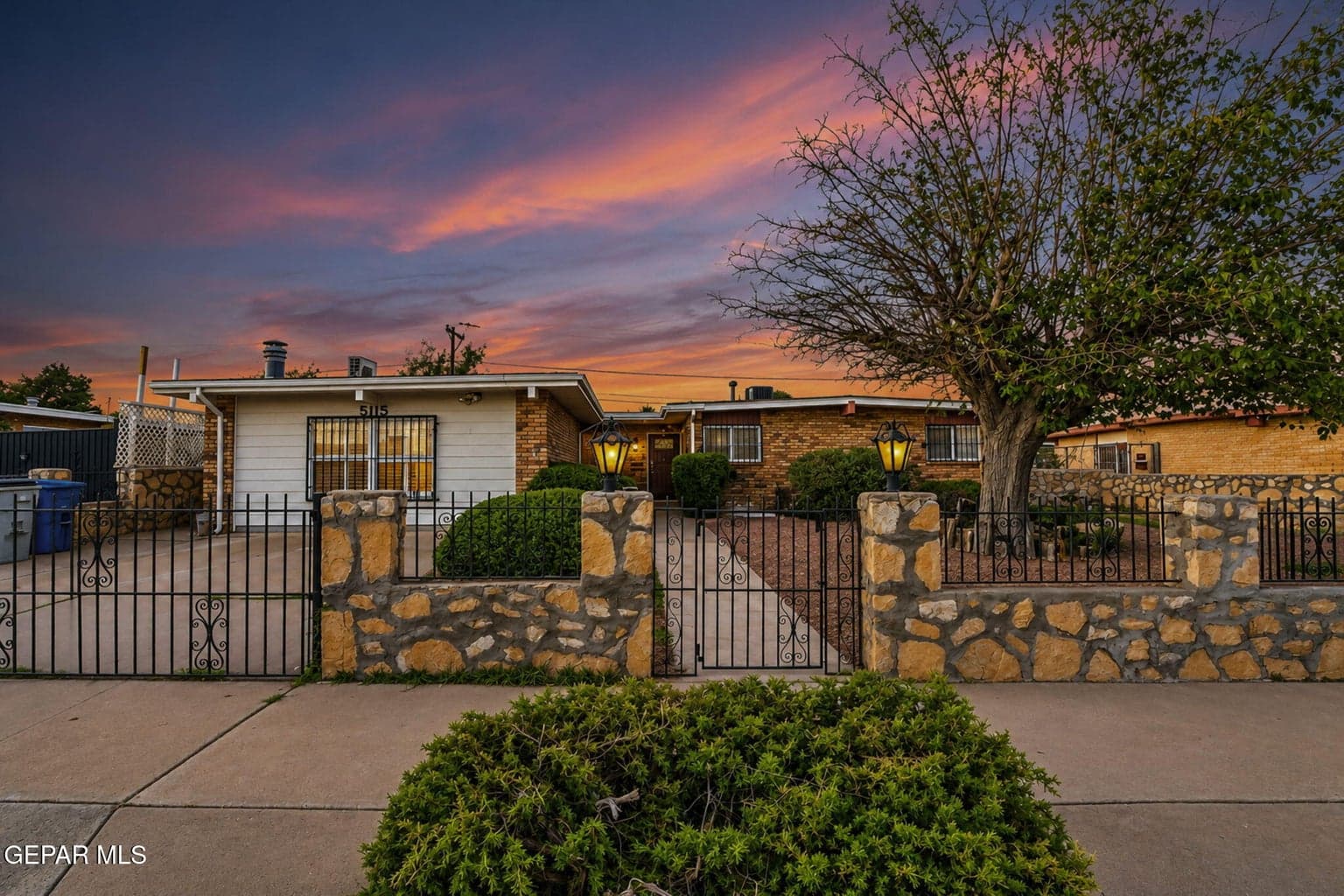 Single-story exterior featuring a brick and horizontal siding facade, complemented by a front yard enclosed with custom wrought iron fencing and masonry stone pillars