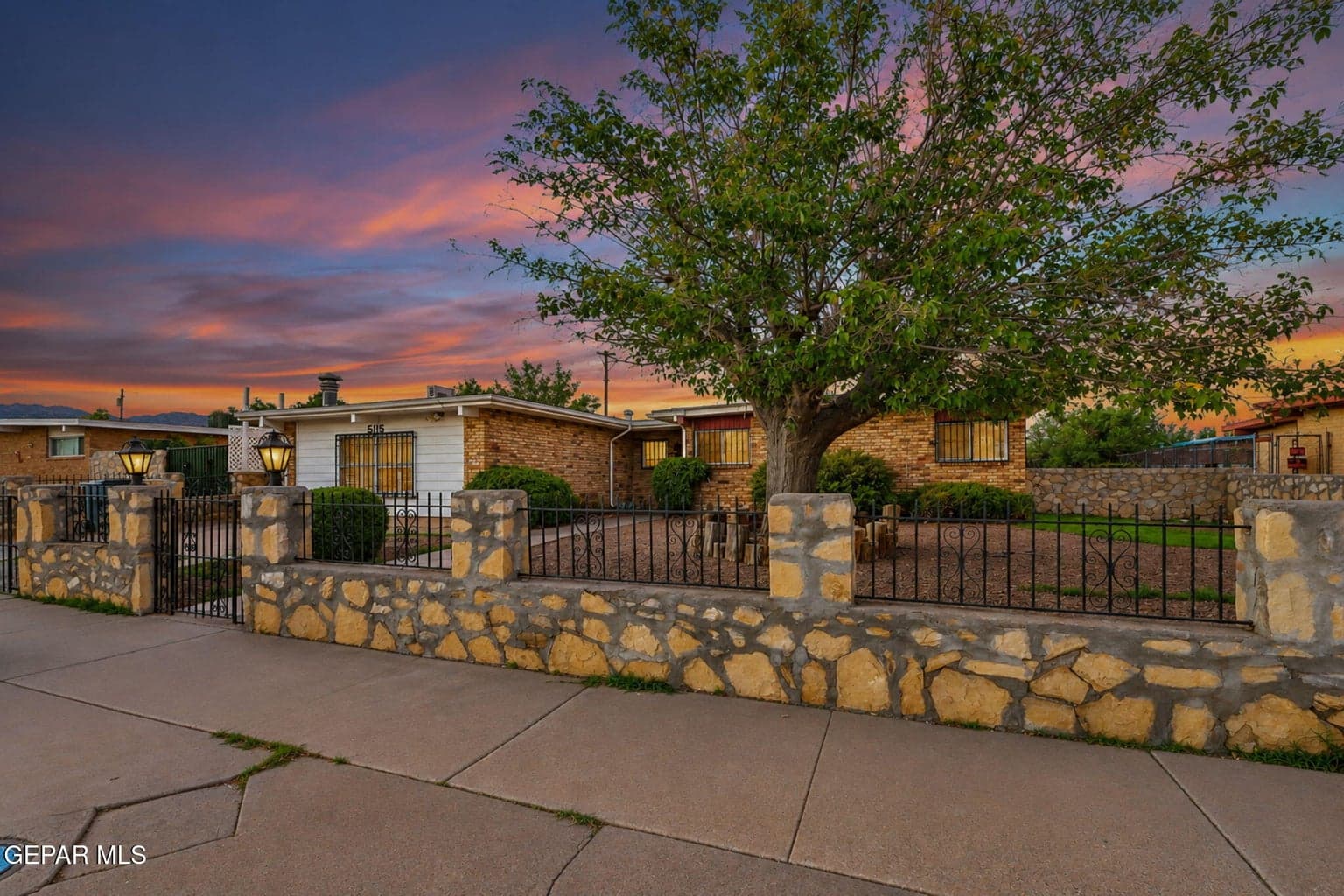 Exterior featuring a brick and stone facade, a decorative stone perimeter wall with integrated iron fencing, and a large mature tree