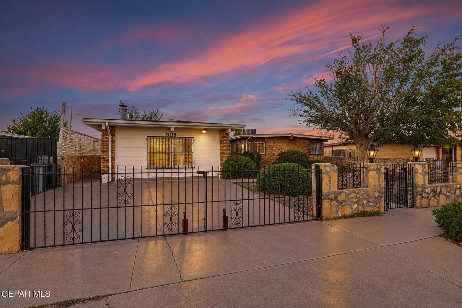 Exterior facade featuring horizontal siding and brick accents, concrete driveway, stone perimeter wall, and decorative metal security fencing