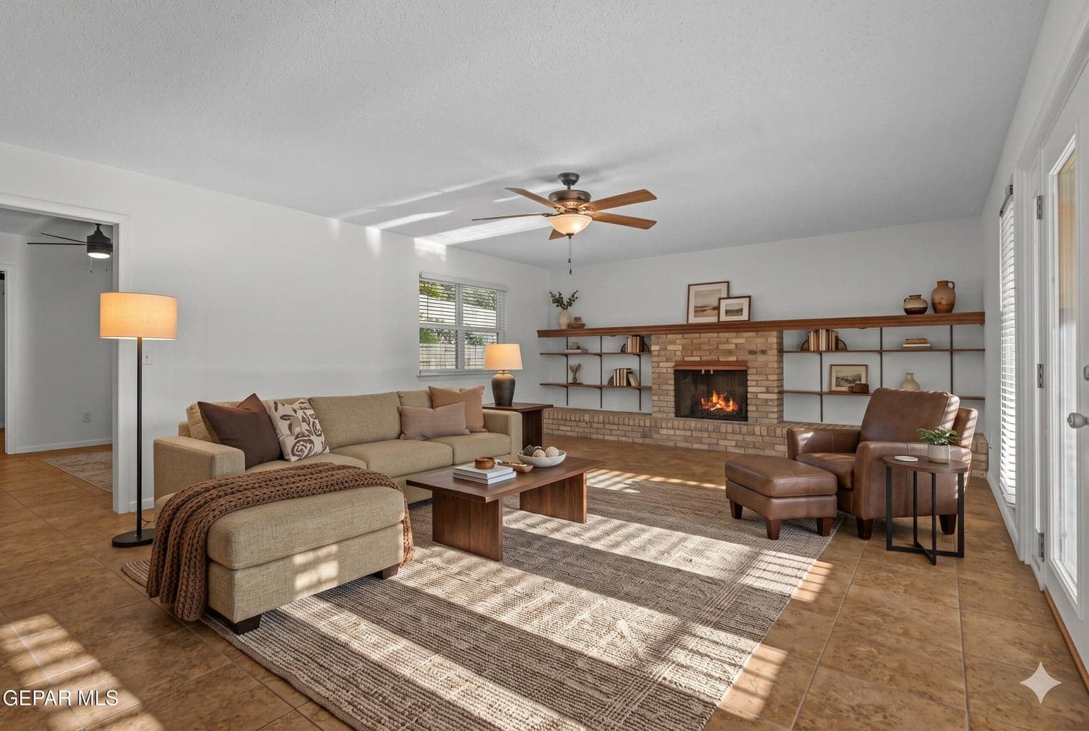 Enjoy a generous gathering space featuring tile flooring, a ceiling fan, and a cozy fireplace.