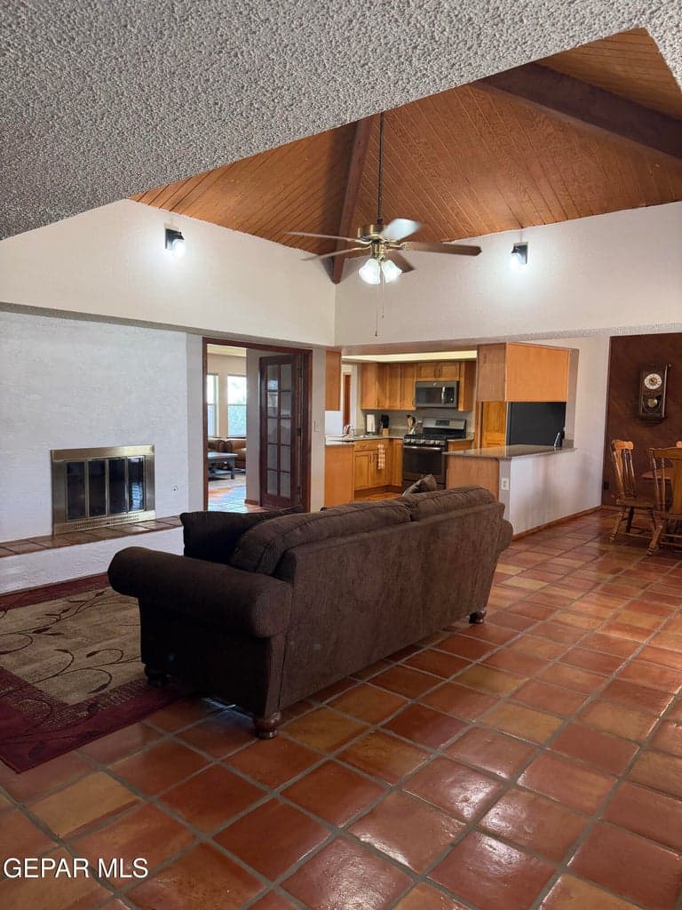 Vaulted wood-paneled ceiling with exposed structural beam, ceramic tile flooring, built-in fireplace with tile hearth, and wood cabinetry